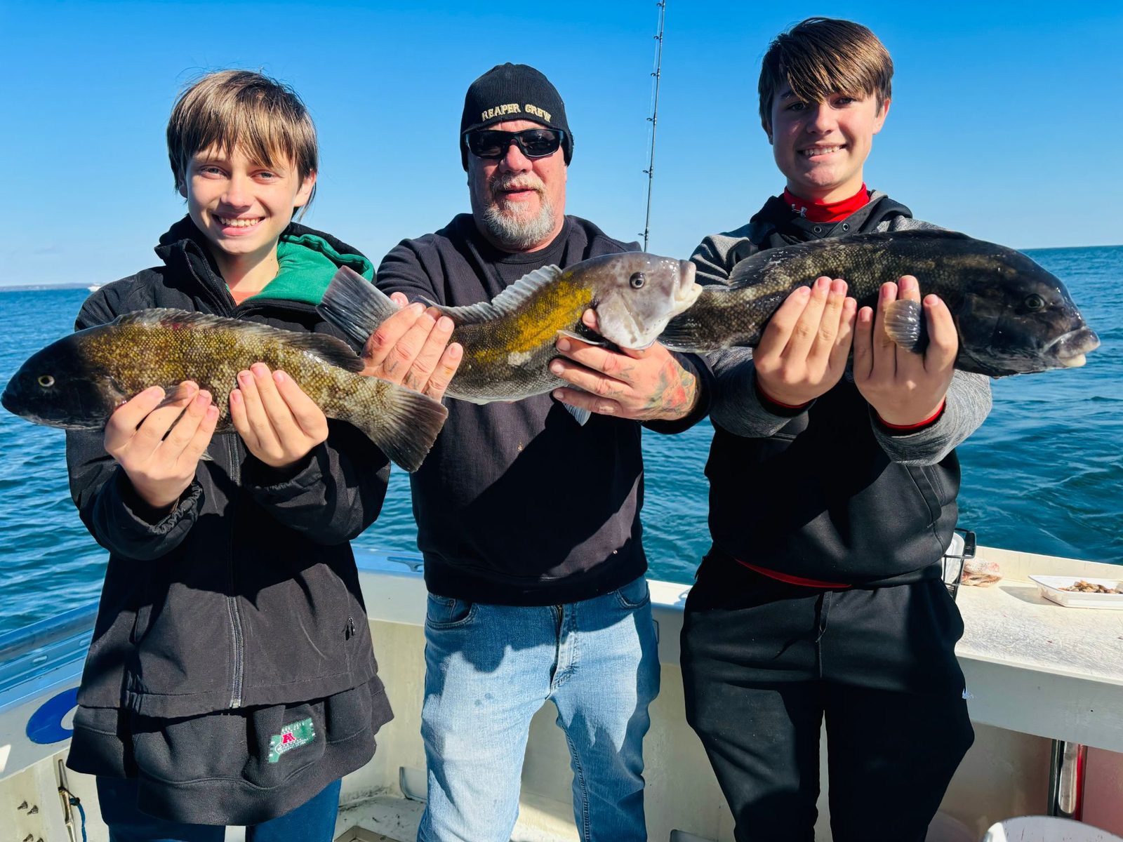 Two young anglers and a man each holding a blackfish on Long Island Sound