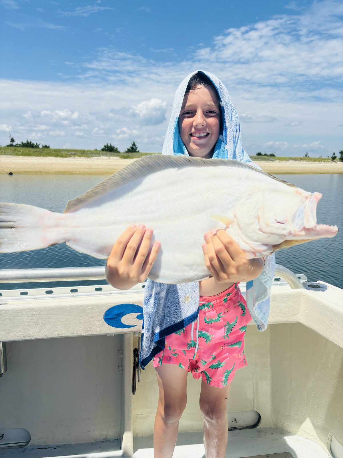 A young angler wrapped in a towel, holding a fluke