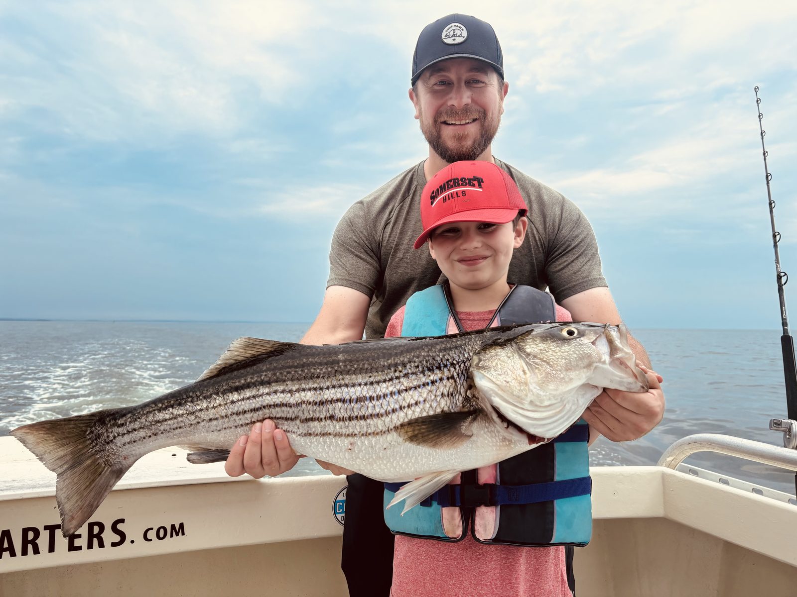 An angler and a boy in a life jacket with a striped bass