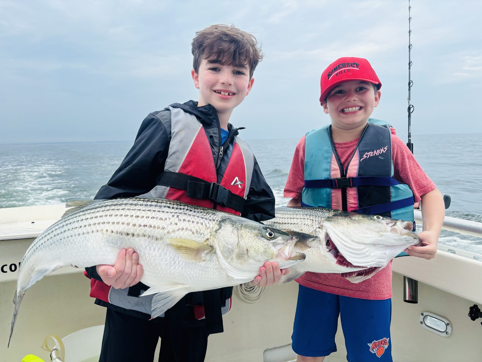 Two kids in life jackets with a striped bass