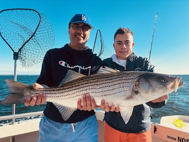 Two anglers holding a long striped bass